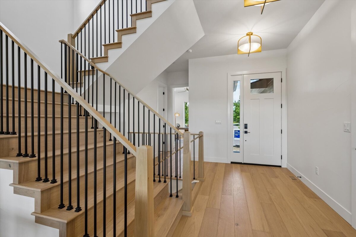light-filled entryway with wood flooring and wood stairs with open handrail