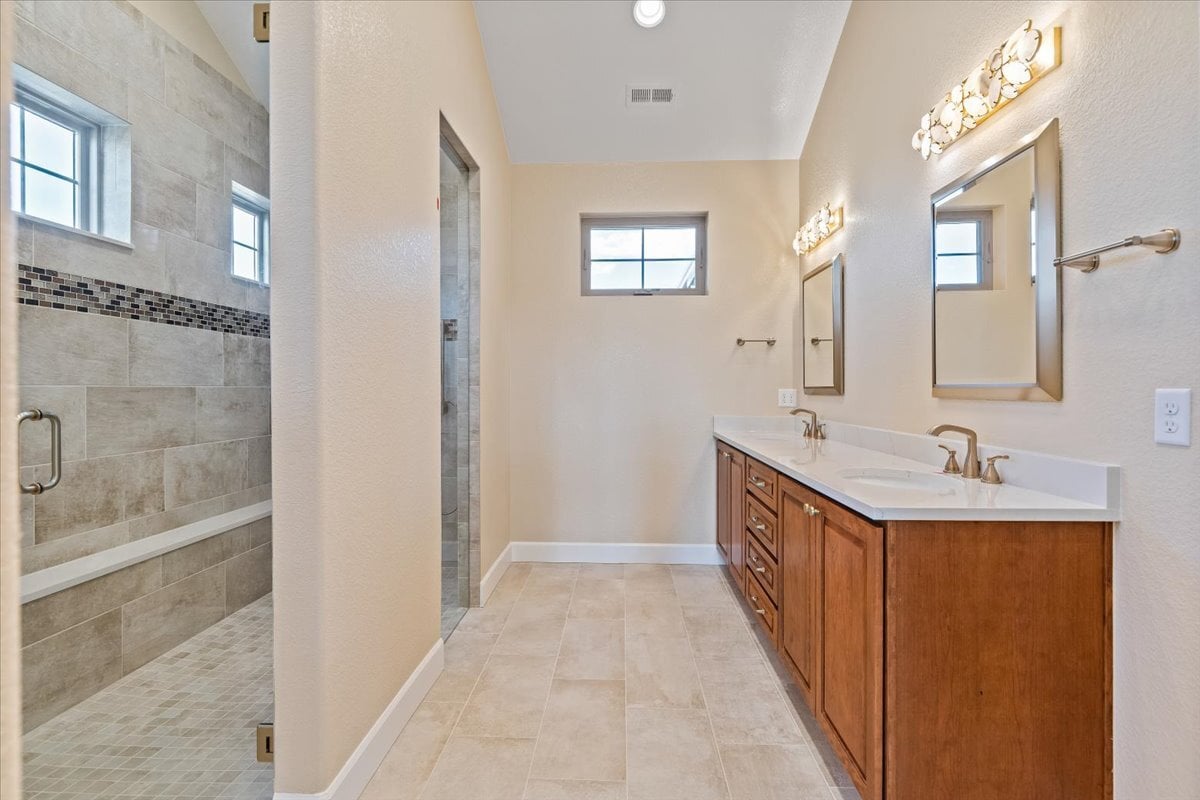primary bath with walk-in tiled shower and double vanity