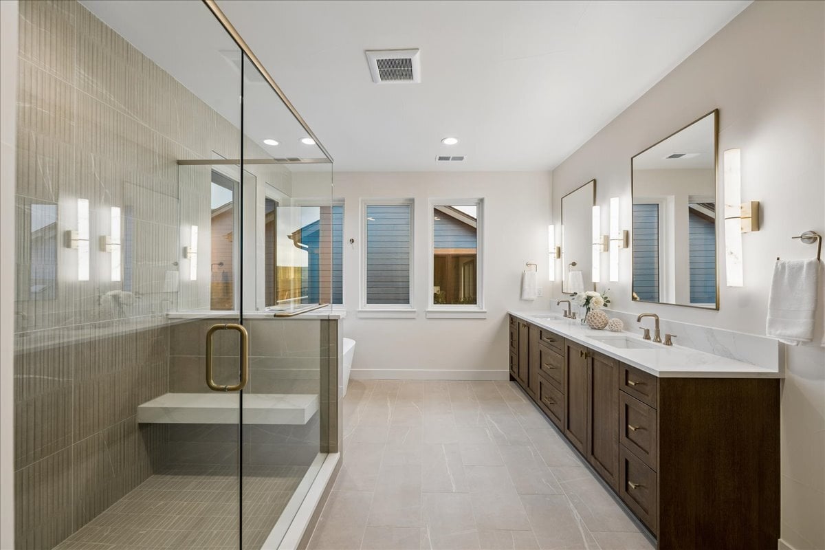 primary bath showing large tiled shower and double vanity with wall sconce lighting