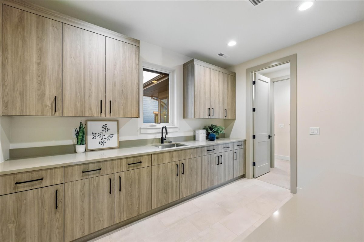 laundry room adjacent to primary suite - features window above laundry sink and wall of built-in cabinetry