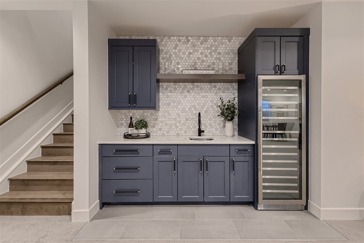 Lower level basement with landing stairs and a wet bar with blue cabinets in a custom home by Sheffield Homes, Franktown, CO