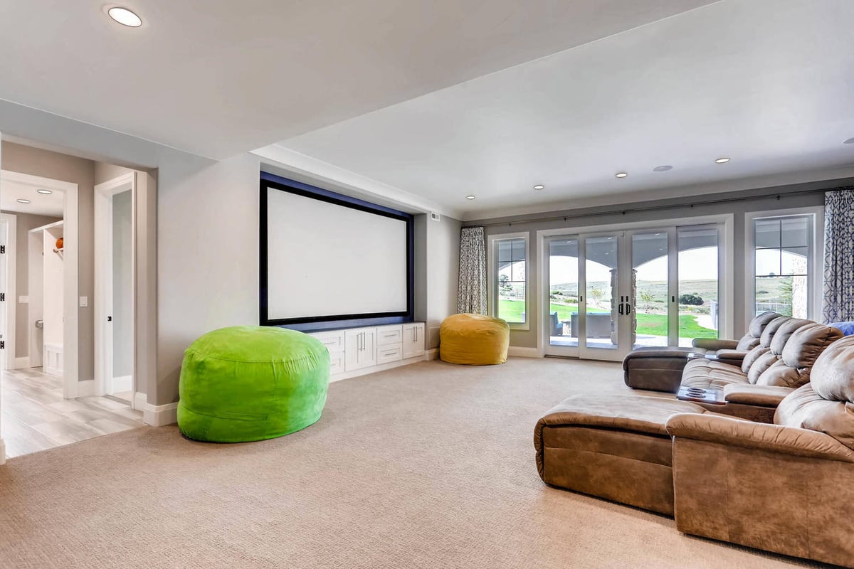 Lower-level spacious family room with carpet flooring and multiple sofa sets in a custom home by Sheffield Homes, Parker, CO