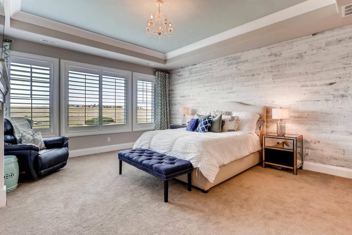 Master bedroom with side table lamps, a single sofa, and sliding windows with curtains in a Sheffield Homes home, Parker, CO