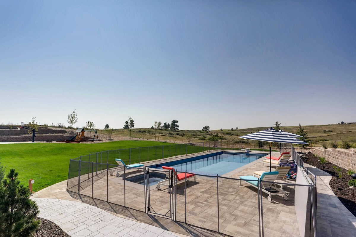Wide-angle shot of the private pool enclosed with a steel mesh fence in a custom home lawn by Sheffield Homes in Parker, CO