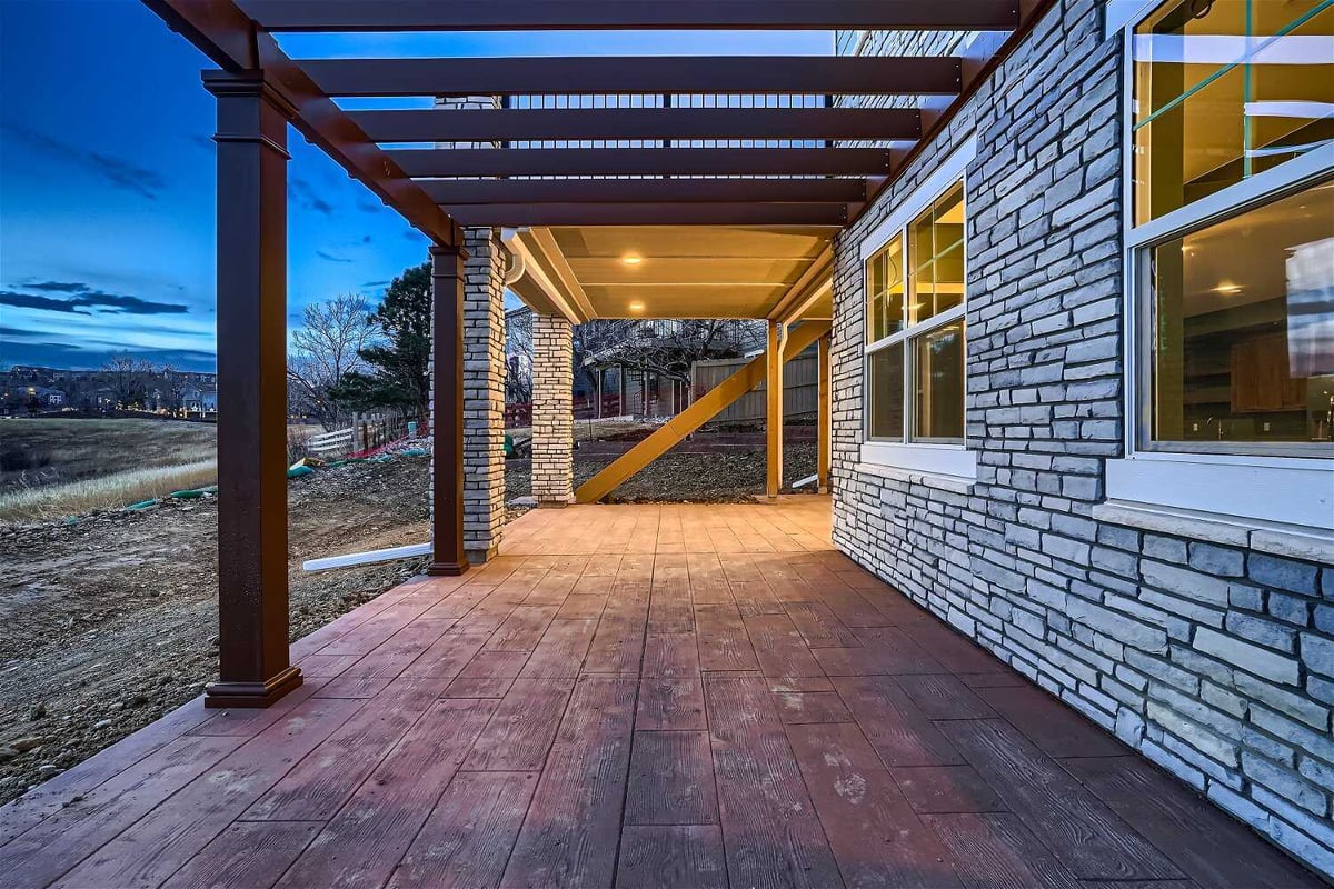 Low-light shot of a custom patio with stone accent wall design and wooden pillars in a Sheffield Homes home in Superior, CO