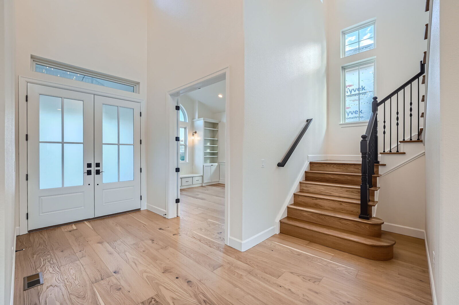 Elegant foyer of a custom-built home by Sheffield Homes in Denver, CO, featuring light wood flooring, double doors, and a staircase with iron railing