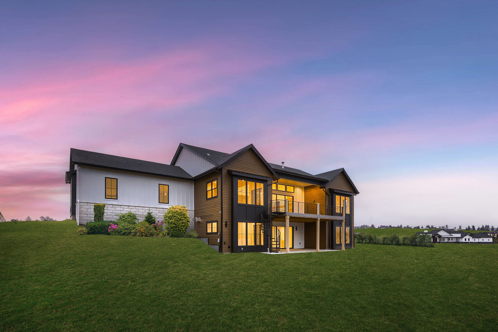 Rear view of a custom home by Sheffield Homes in Denver, CO, showcasing a large deck and expansive lawn under a serene evening sky