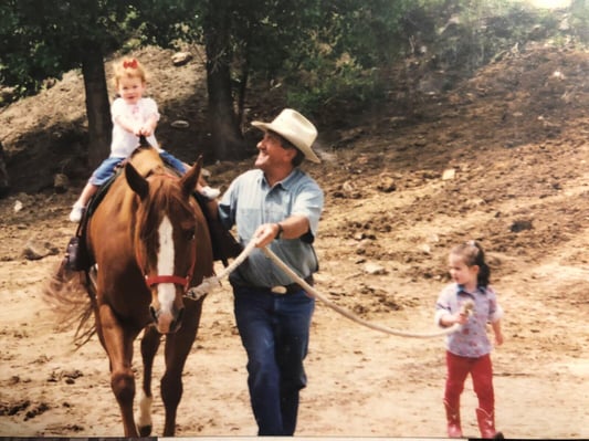 john leading a horse with two young girls, one riding and one walking beside, in a rural setting