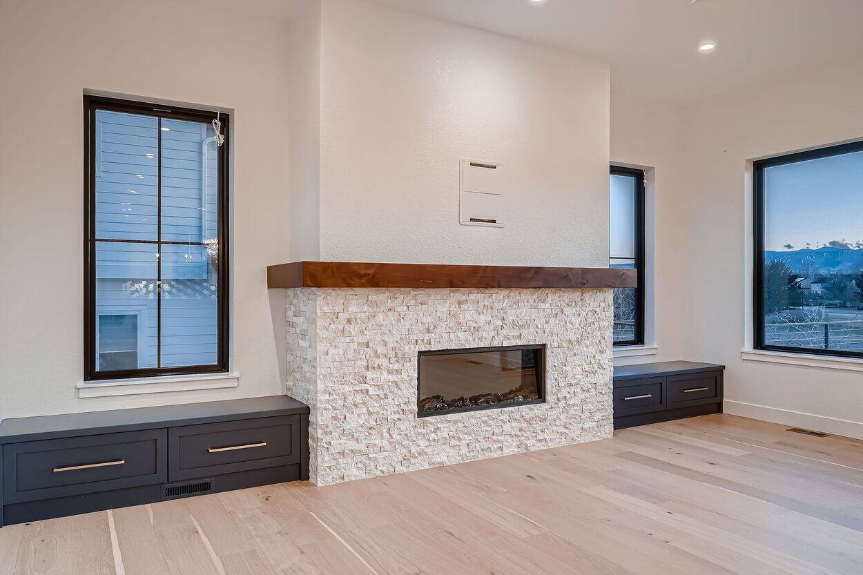 Stone fireplace with wood mantle between black-framed windows in a custom home by Sheffield Homes in Denver, CO