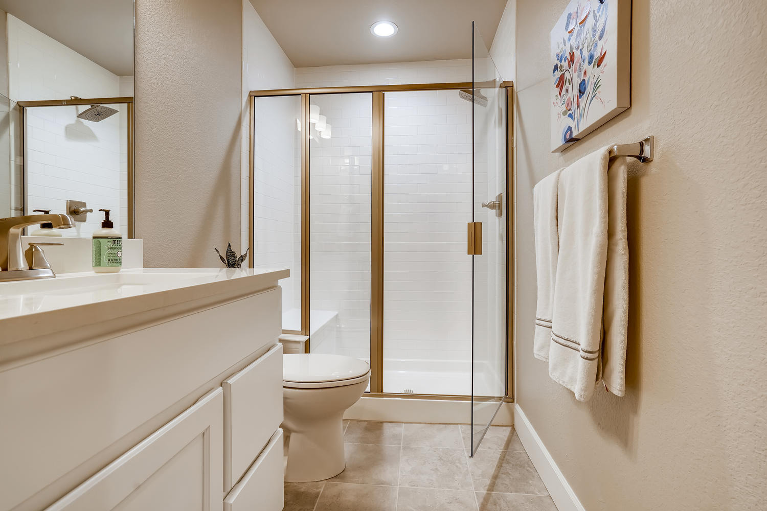 Stylish bathroom remodel with white cabinets and glass-enclosed shower, basement finishing project by Sheffield Homes in Arvada, CO