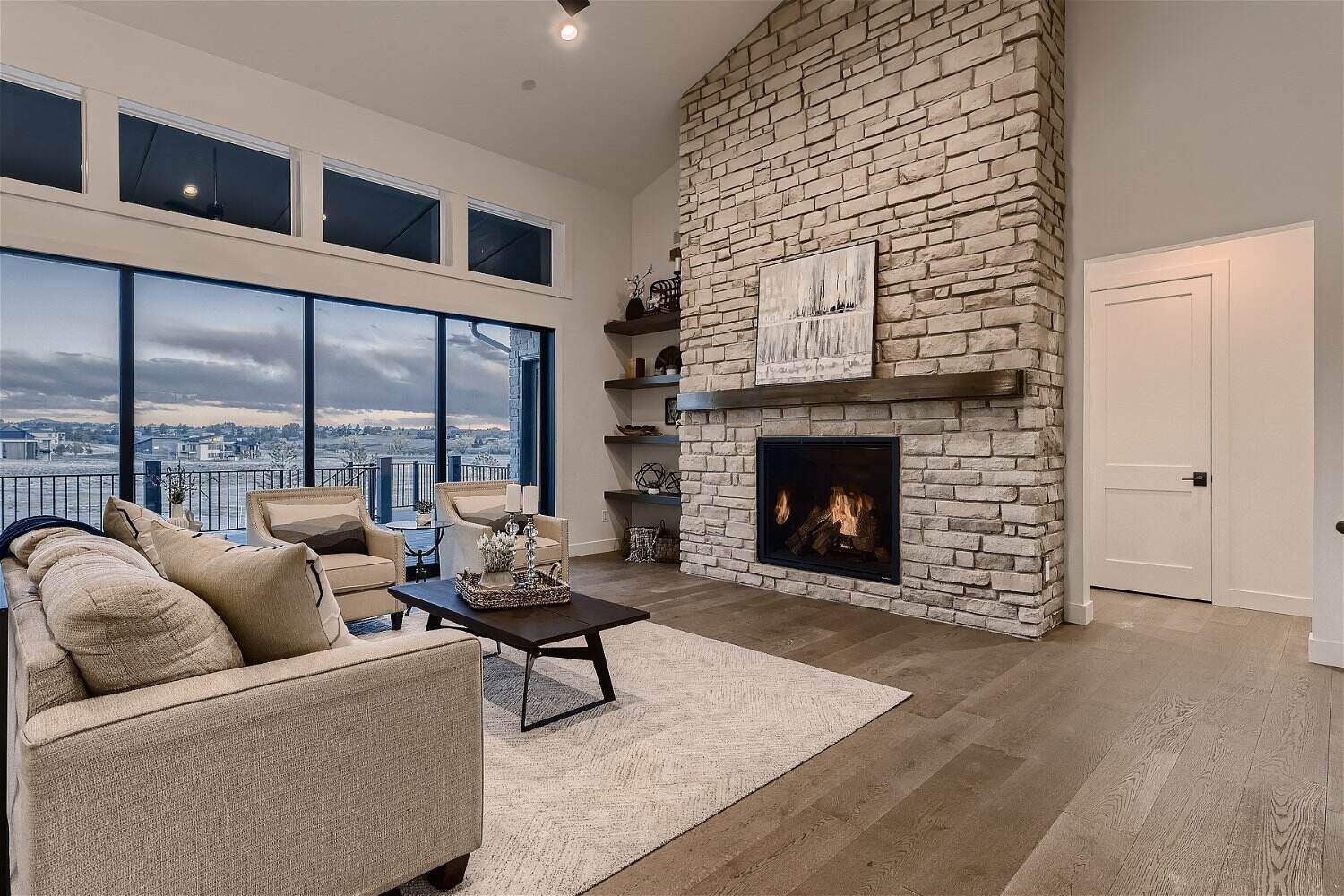 Living room with sofas and a table in front of a stone wall with a mounted fireplace by Sheffield Homes in Franktown, CO