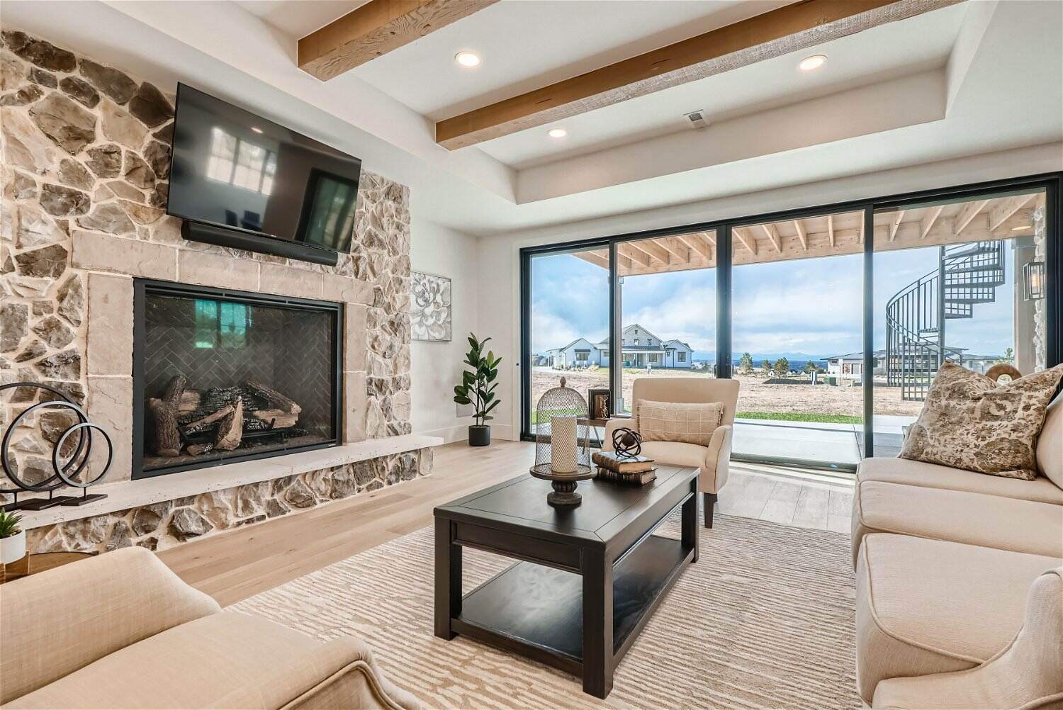 Cozy lower-level family room in a custom Denver home by Sheffield Homes, featuring a stone fireplace, rustic wood beams, and expansive sliding glass doors Cozy lower-level family room in a custom Denver home by Sheffield Homes, featuring a stone fireplace, rustic wood beams, and expansive sliding glass doors